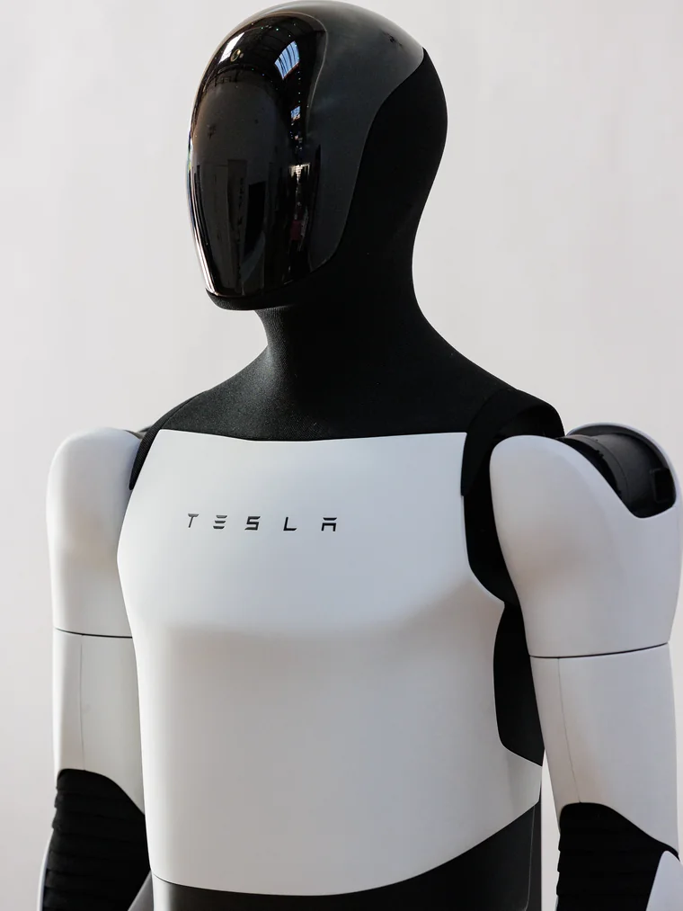 A Tesla Optimus humanoid robot standing against a white wall