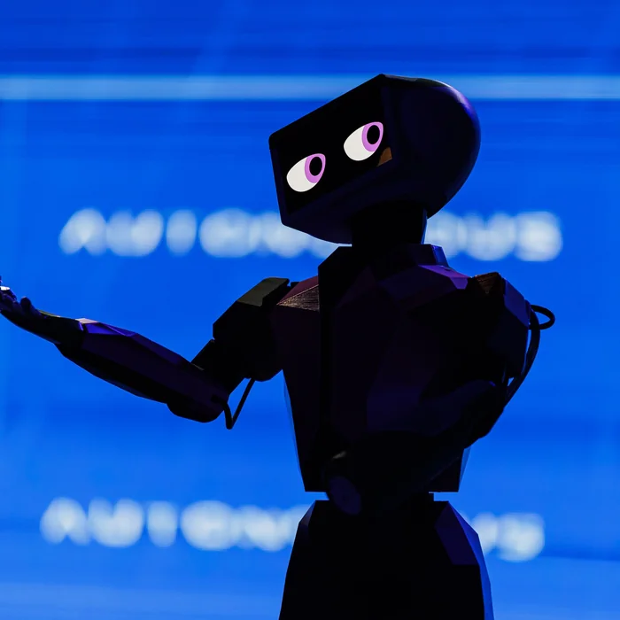 A humanoid robot on stage, arm raised, against the AUTONOMOUS backdrop
